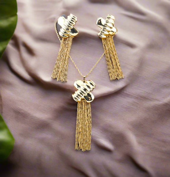 Gold jewelry set with abstract hammered pendant and matching tassel earrings displayed on black bust stand
