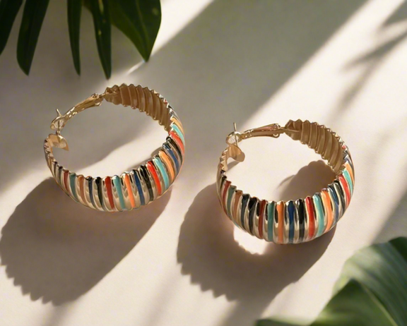 Gold hoop earrings with multicolor enamel stripes, displayed on a book page with pink roses in the background.