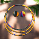 Ankara fabric-wrapped triple-strand necklace in bold red, yellow, green, and blue with matching round African print button earrings displayed on a black bust stand.