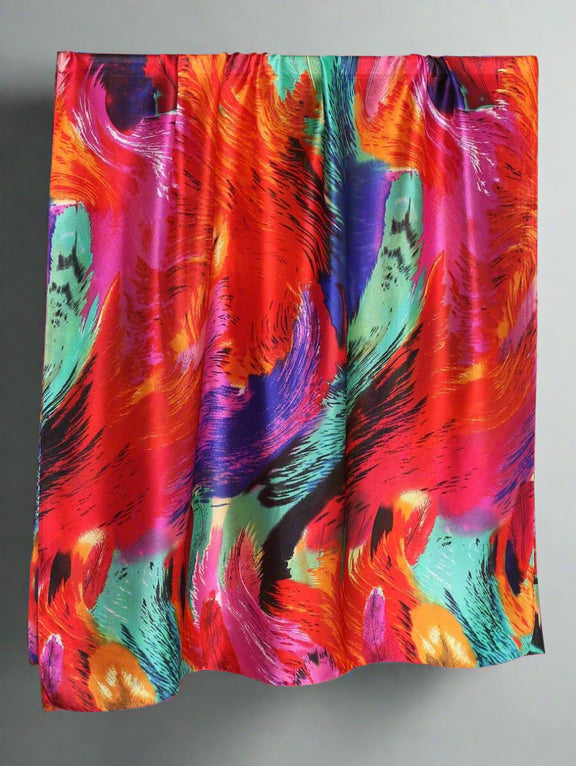 A luxurious silk scarf with a vibrant abstract design featuring bold red, blue, green, and orange hues. The fabric has a glossy finish, draping elegantly for a statement look.