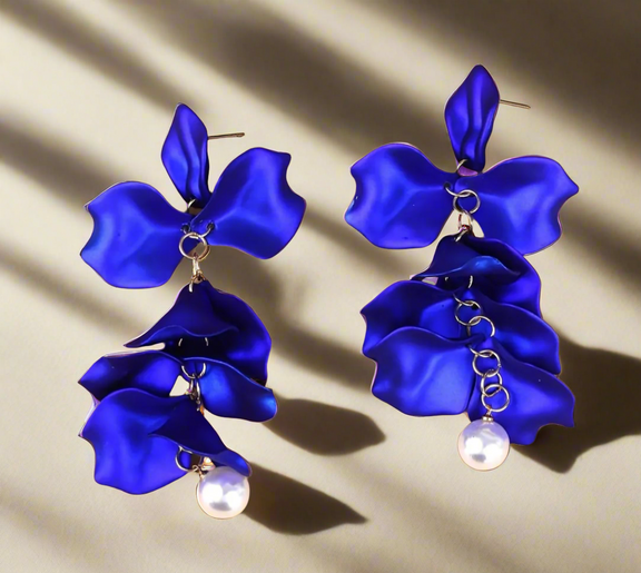 Elegant long drop earring featuring layered royal blue polymer clay petals and a pearl bead at the bottom, worn on a model with blonde hair.