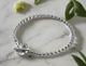 Close-up of a men’s stainless steel bracelet with a toggle clasp featuring an engraved circular design, worn on wrist.