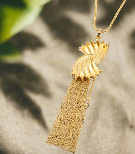 Gold sculpted swirl tassel necklace with a long chain and elegant fringe detail, displayed on a white background with text