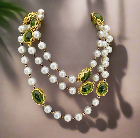 Long layered necklace featuring alternating white pearl beads and oval green gemstones framed in gold-tone settings, displayed on a black velvet bust. The necklace can be worn as a single long strand or wrapped into a double-layered style.