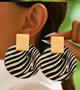 A close-up of a person wearing statement Phanie earrings from the Desiree W.A.R Store, featuring bold zebra prints with large circular designs and rectangular gold-colored tops, crafted from lightweight faux leather.
