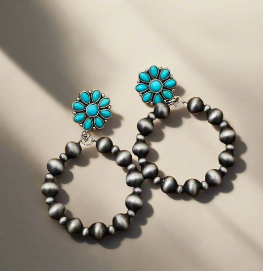 Turquoise floral and antique silver beaded hoop earrings displayed on a cowhide background, perfect for Western and boho-chic fashion.