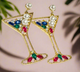 A pair of glamorous martini glass-shaped earrings with a gold-tone finish, adorned with colorful rhinestones and pearl embellishments, hanging elegantly against a neutral background.