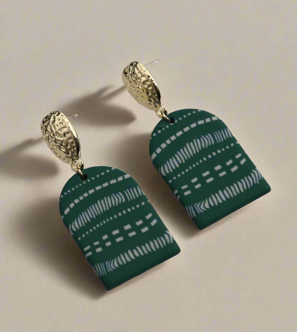 A pair of handcrafted statement earrings featuring gold-tone hammered metal studs with teal-green arched pendants adorned with white tribal patterns, designed for bold, elegant styling
