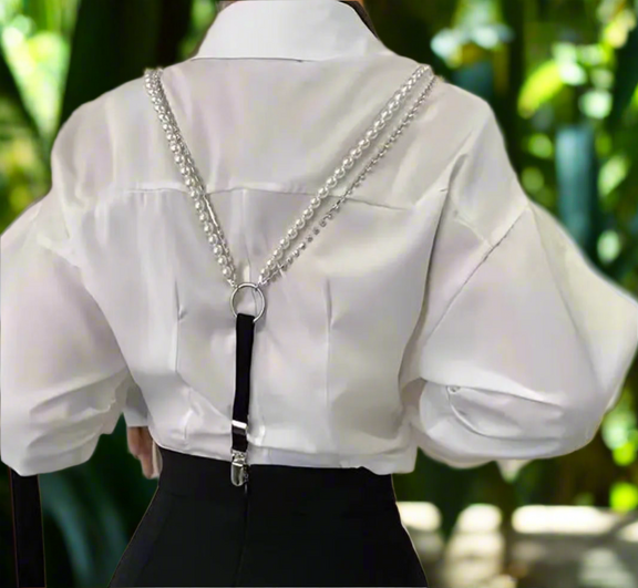 Pearl and black suspender straps clipped to black pants and styled over a white satin blouse for a modern, elegant look.