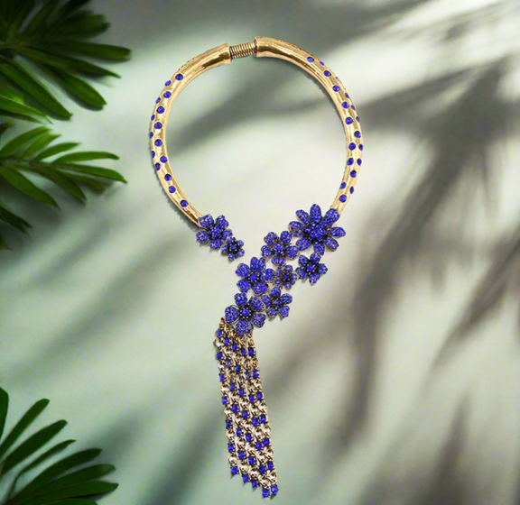 Bold vintage gold statement necklace featuring sapphire blue floral accents and cascading chain tassels, displayed on a black mannequin bust