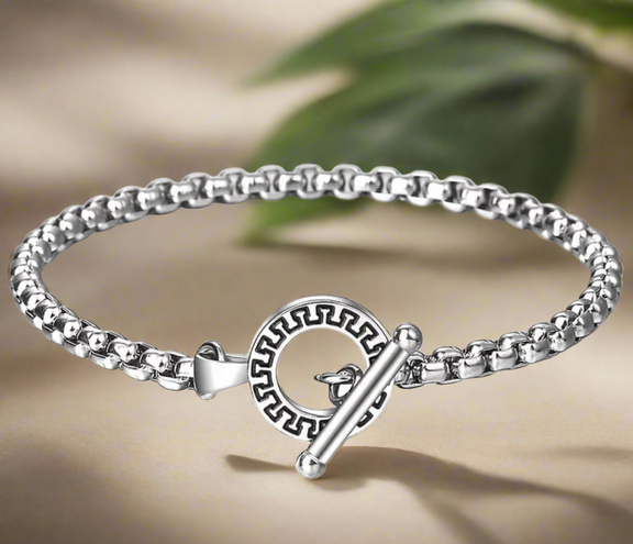 Close-up of a men’s stainless steel bracelet with a toggle clasp featuring an engraved circular design, worn on wrist.
