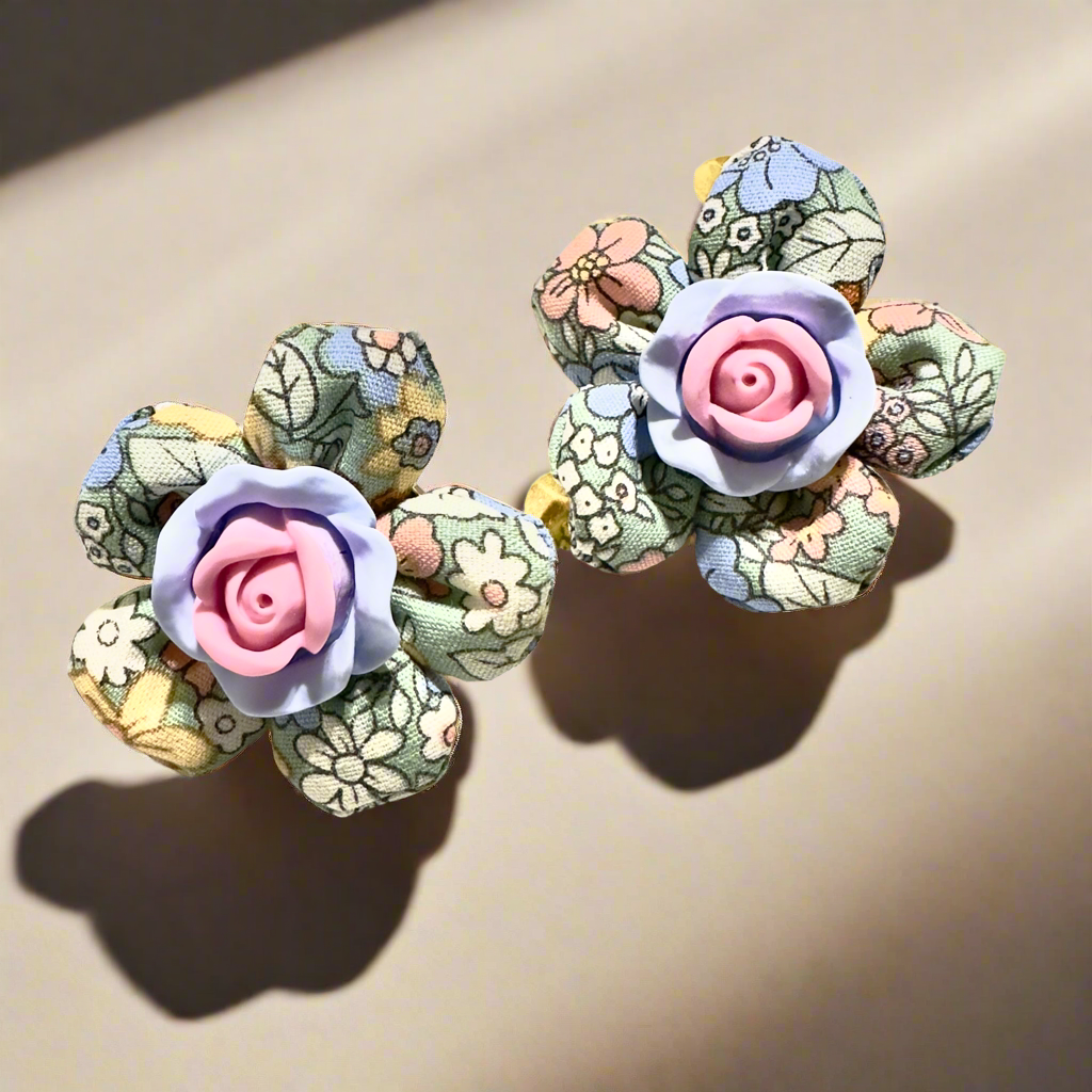 Handmade floral fabric earrings with pastel petals and a pink resin rose centerpiece, displayed on a white background with gold polka dots.