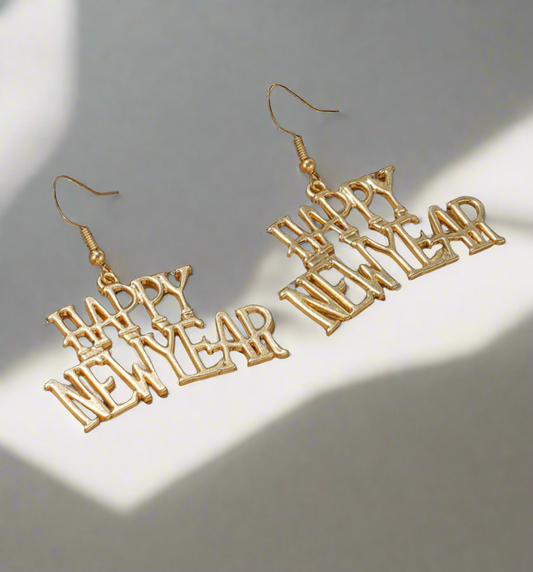 The 2025 New You! gold earrings from Desiree W.A.R Store feature a festive Happy New Year design with hooks, displayed against a light background with shadows.