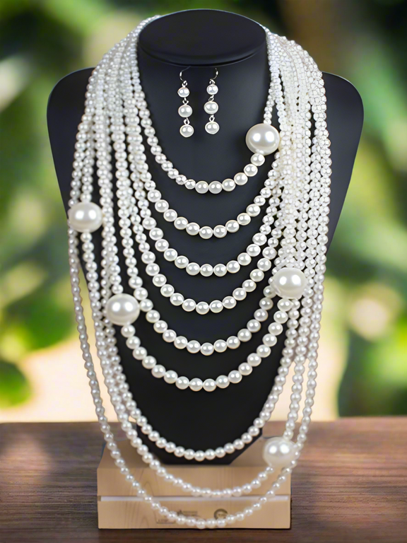 A luxurious looking  multi-layered pearl necklace displayed on a black bust stand, featuring cascading strands of white pearls in varying sizes with matching pearl drop earrings.
