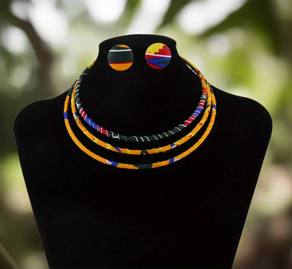Ankara fabric-wrapped triple-strand necklace in bold red, yellow, green, and blue with matching round African print button earrings displayed on a black bust stand.