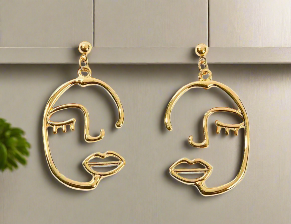 The La Muse earrings by Desiree W.A.R Store hang elegantly on a display board, showcasing modern abstract art through their golden minimalist design and artistic features.