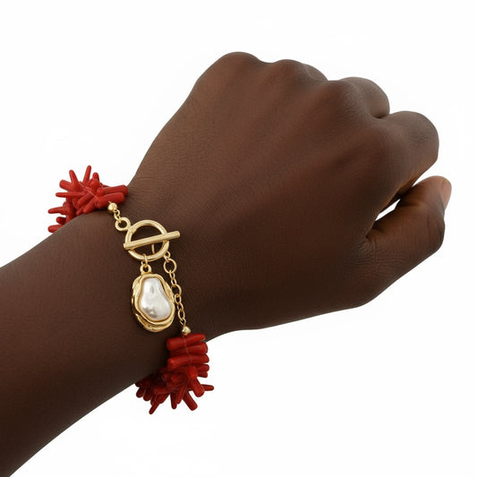 Hand wearing a gold bracelet with red coral-like charms on a white background