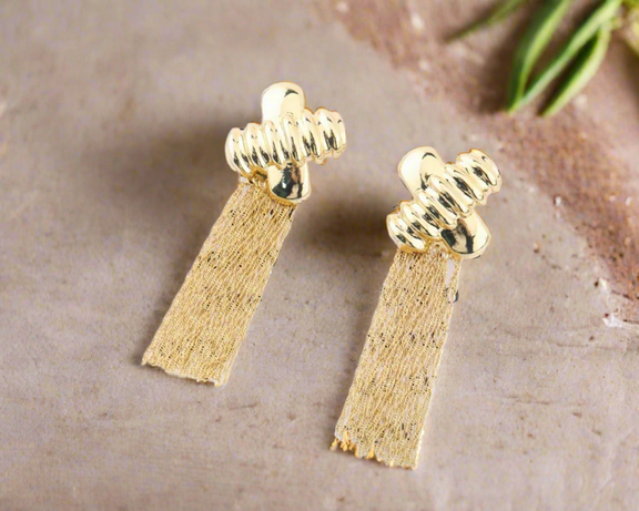 Gold jewelry set with abstract hammered pendant and matching tassel earrings displayed on black bust stand