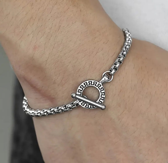 Close-up of a men’s stainless steel bracelet with a toggle clasp featuring an engraved circular design, worn on wrist.