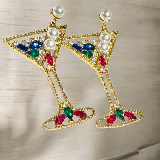 A pair of glamorous martini glass-shaped earrings with a gold-tone finish, adorned with colorful rhinestones and pearl embellishments, hanging elegantly against a neutral background.