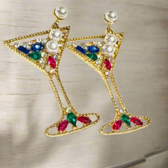 A pair of glamorous martini glass-shaped earrings with a gold-tone finish, adorned with colorful rhinestones and pearl embellishments, hanging elegantly against a neutral background.