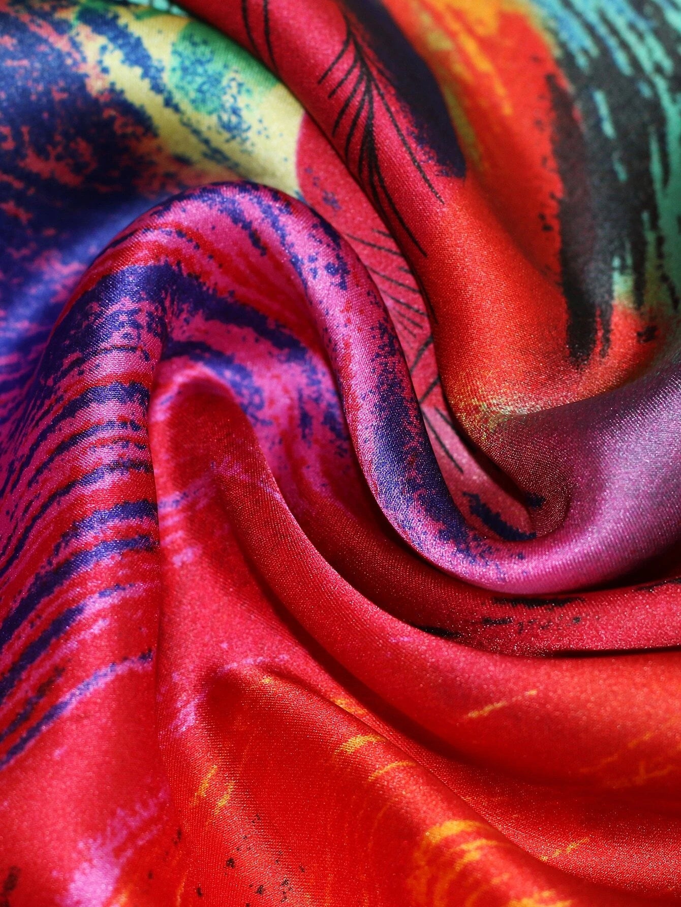 A luxurious silk scarf with a vibrant abstract design featuring bold red, blue, green, and orange hues. The fabric has a glossy finish, draping elegantly for a statement look.