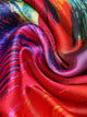 A luxurious silk scarf with a vibrant abstract design featuring bold red, blue, green, and orange hues. The fabric has a glossy finish, draping elegantly for a statement look.