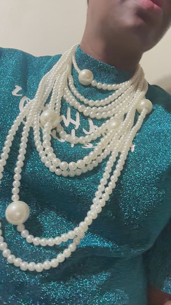 A luxurious looking  multi-layered pearl necklace displayed on a black bust stand, featuring cascading strands of white pearls in varying sizes with matching pearl drop earrings.