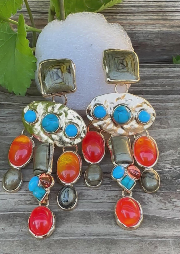 Colorful dangle earrings with gold backing, featuring orange, turquoise, and olive-green stones in various shapes and sizes arranged in a cascading design.
