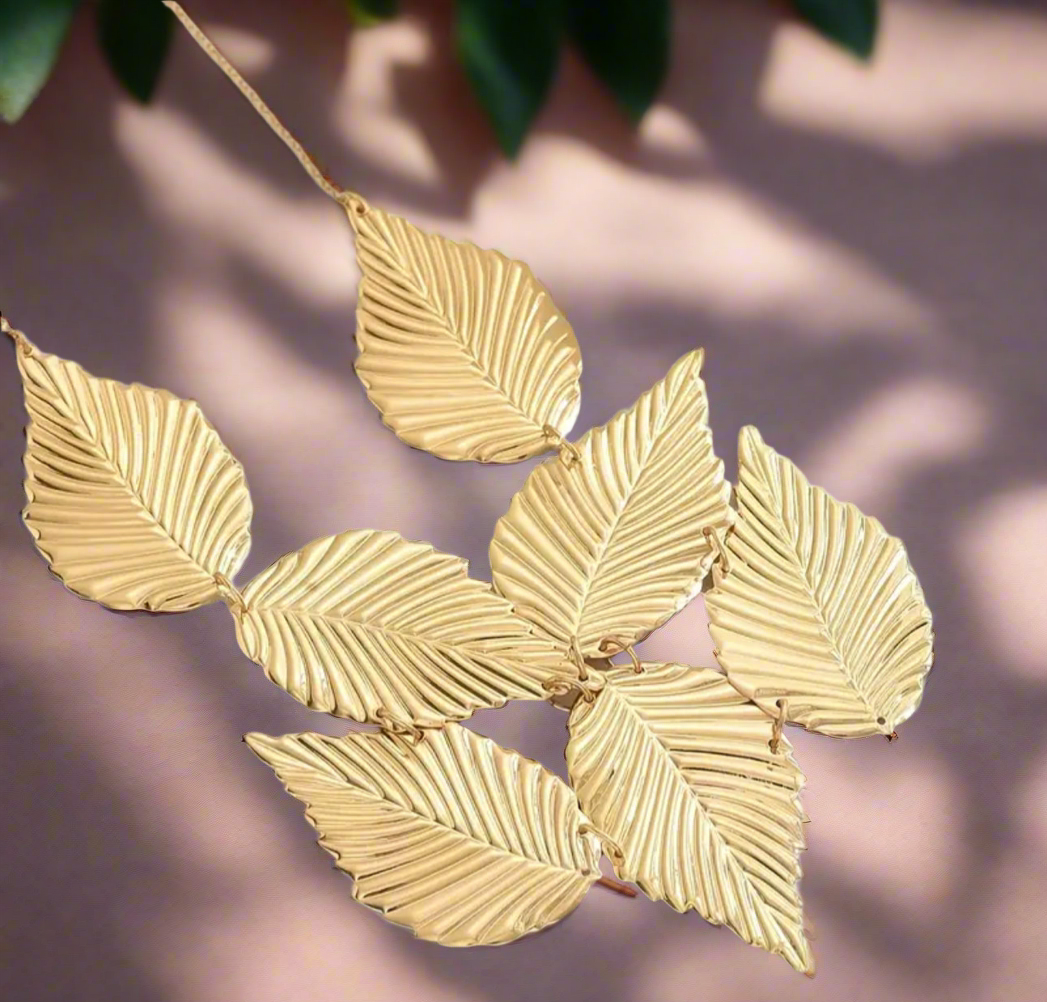 Close-up of the Gladys Golden Leaves Necklace featuring seven large, textured gold leaves arranged in a fan shape on a gold chain, displayed on a neutral background
