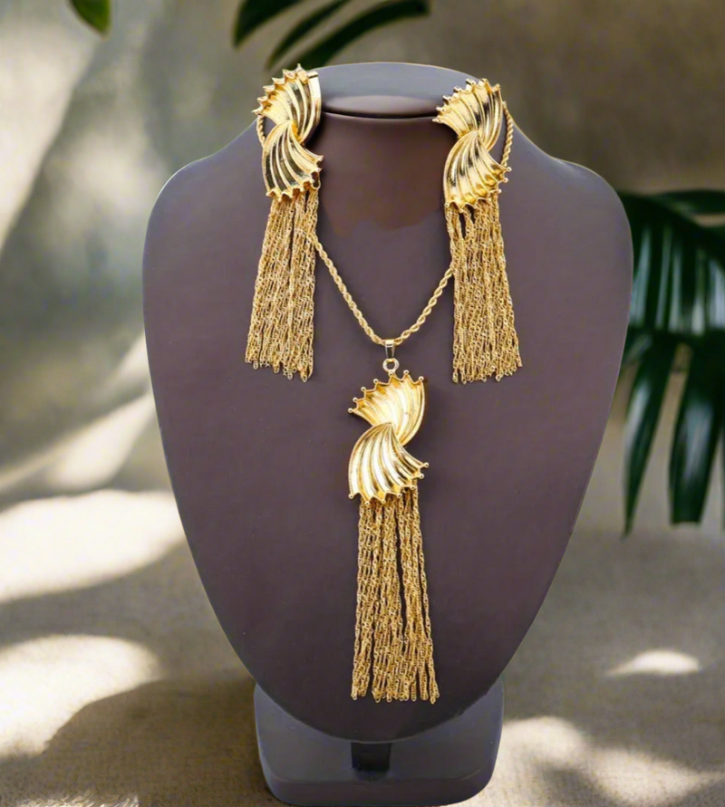 Gold sculpted swirl tassel necklace with a long chain and elegant fringe detail, displayed on a white background with text