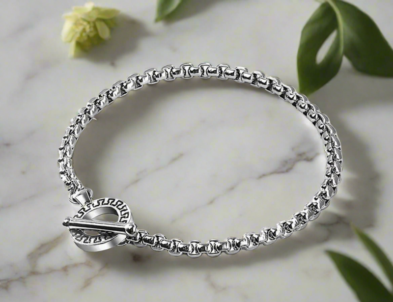 Close-up of a men’s stainless steel bracelet with a toggle clasp featuring an engraved circular design, worn on wrist.