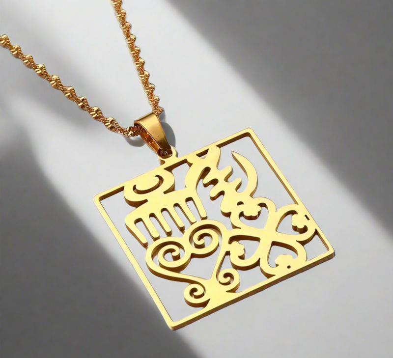 A gold-plated necklace featuring a square-shaped pendant with intricate cultural patterns, displayed on a textured gold chain against a softly lit background.