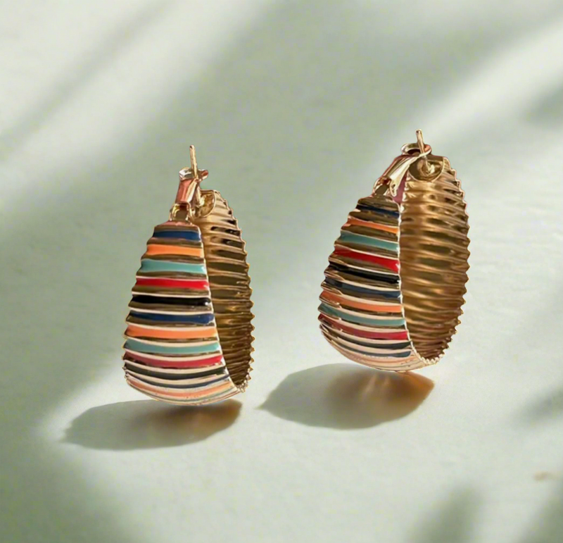 Gold hoop earrings with multicolor enamel stripes, displayed on a book page with pink roses in the background.