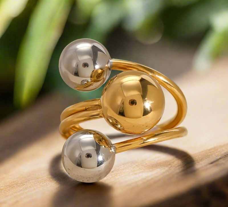Gold and silver orbit-style statement ring with three polished spheres on a wrap band