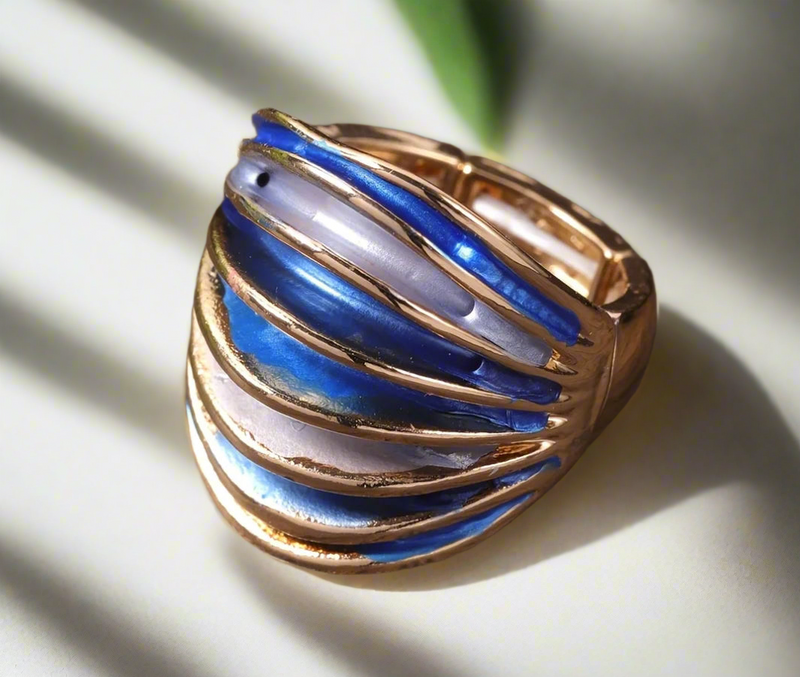 Bold gold statement ring with curved blue and pearl-toned enamel accents, placed on a wooden surface.