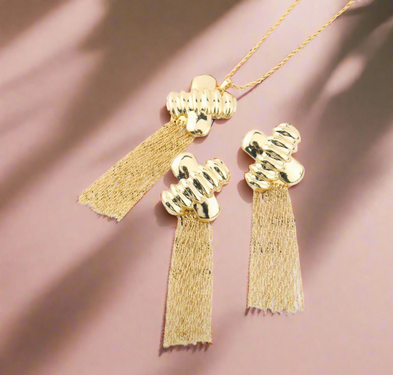Gold jewelry set with abstract hammered pendant and matching tassel earrings displayed on black bust stand