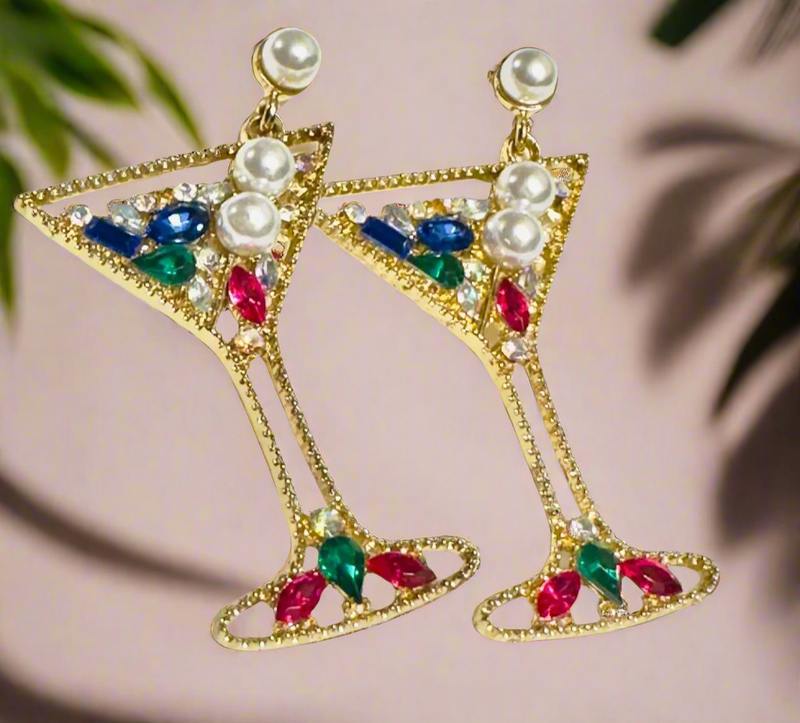 A pair of glamorous martini glass-shaped earrings with a gold-tone finish, adorned with colorful rhinestones and pearl embellishments, hanging elegantly against a neutral background.