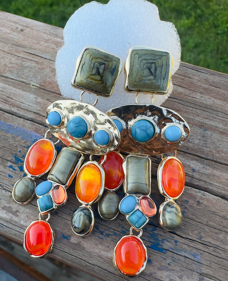 Colorful dangle earrings with gold backing, featuring orange, turquoise, and olive-green stones in various shapes and sizes arranged in a cascading design.