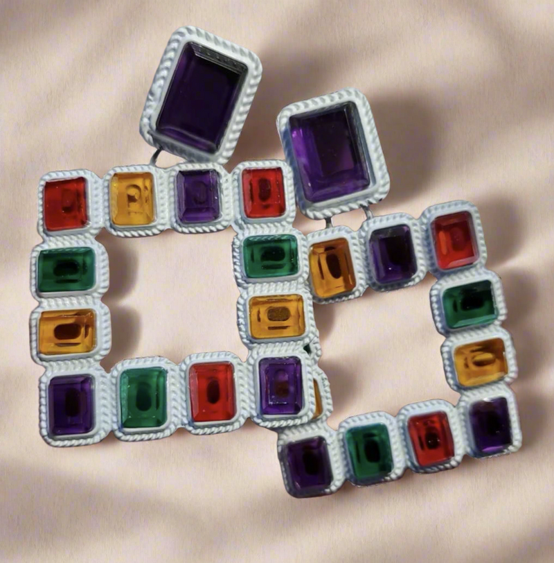 Vibrant geometric square earrings featuring multicolored red, green, purple, and yellow gemstones set in a textured white frame – a bold statement accessory