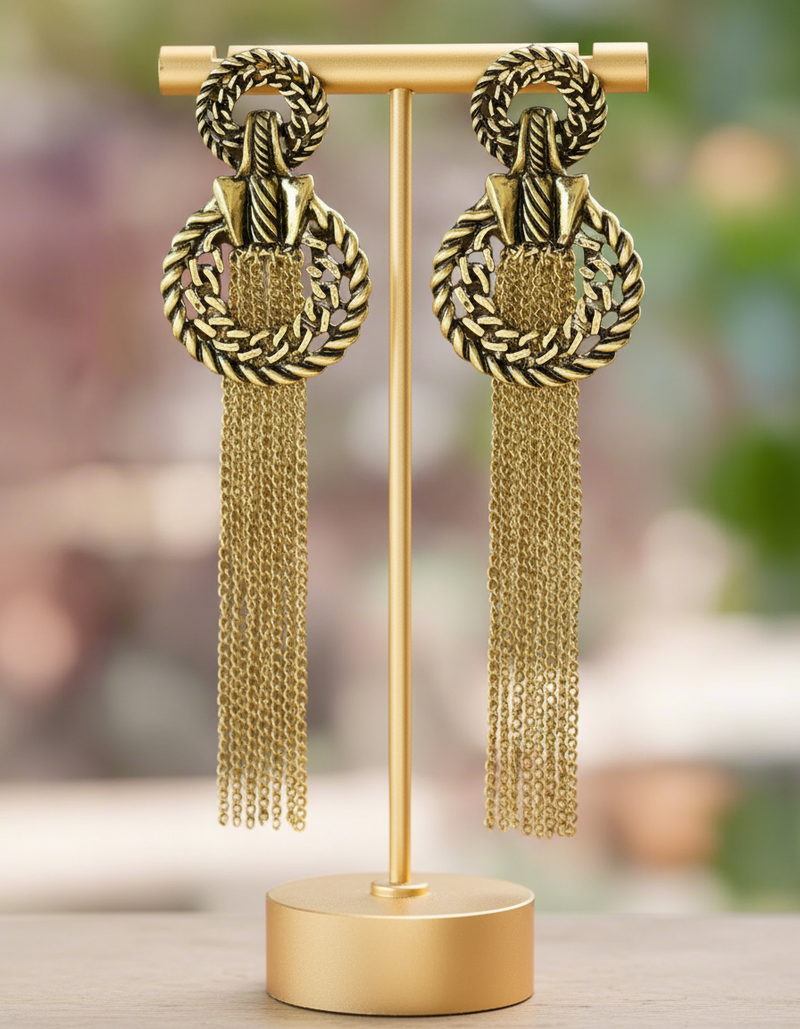 Pair of gold earrings with braided design and tassels on a blurred background