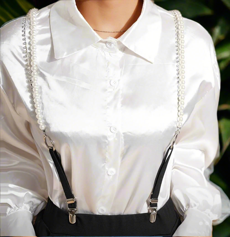 Pearl and black suspender straps clipped to black pants and styled over a white satin blouse for a modern, elegant look.