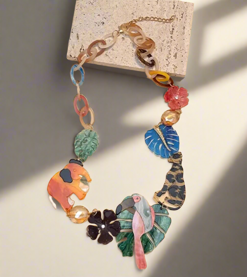 Colorful jungle-themed statement necklace with resin charms of a pink flamingo, orange elephant, leopard, tropical leaves, and flowers, connected by multicolored acrylic chain links.

