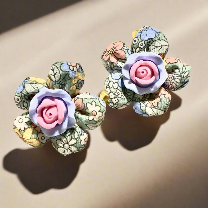 Handmade floral fabric earrings with pastel petals and a pink resin rose centerpiece, displayed on a white background with gold polka dots.