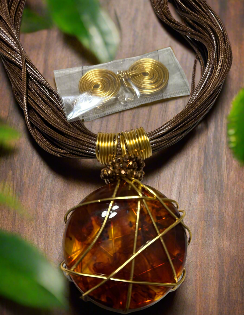 Bold African-inspired amber resin necklace wrapped in gold wire, featuring brown layered cords and matching gold coil earrings, handcrafted jewelry for women.