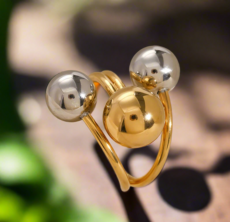 Gold and silver orbit-style statement ring with three polished spheres on a wrap band