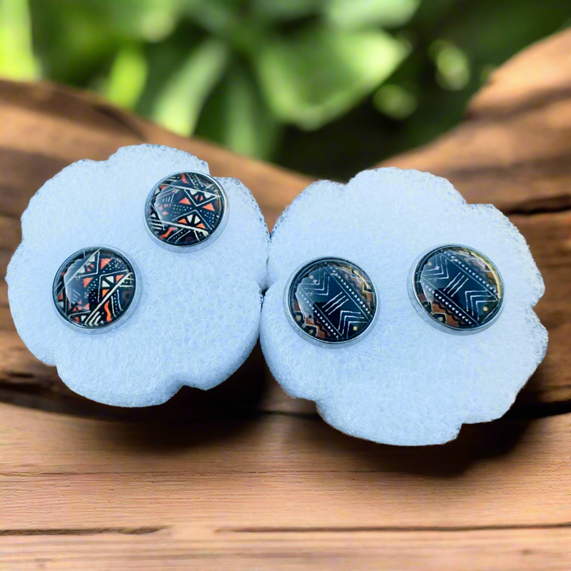 Round stud earrings featuring a bold black, white, and mustard yellow Bogolan-inspired tribal pattern with geometric and zigzag details on a glossy finish.
