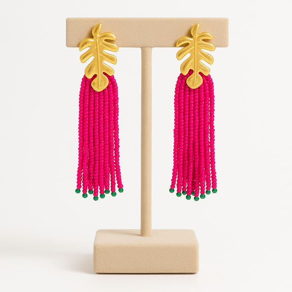 Pink beaded earrings with gold leaf tops on a wooden stand against a white background