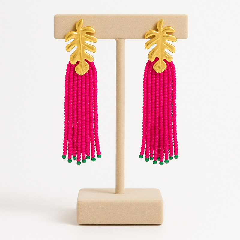 Pink beaded earrings with gold leaf tops on a wooden stand against a white background