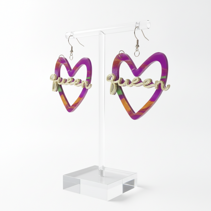 A pair of vibrant, multicolored heart-shaped earrings with the word “Queen” in gold-tone script across the center. The earrings have silver-tone hooks and feature a blend of purple, pink, orange, and green hues.